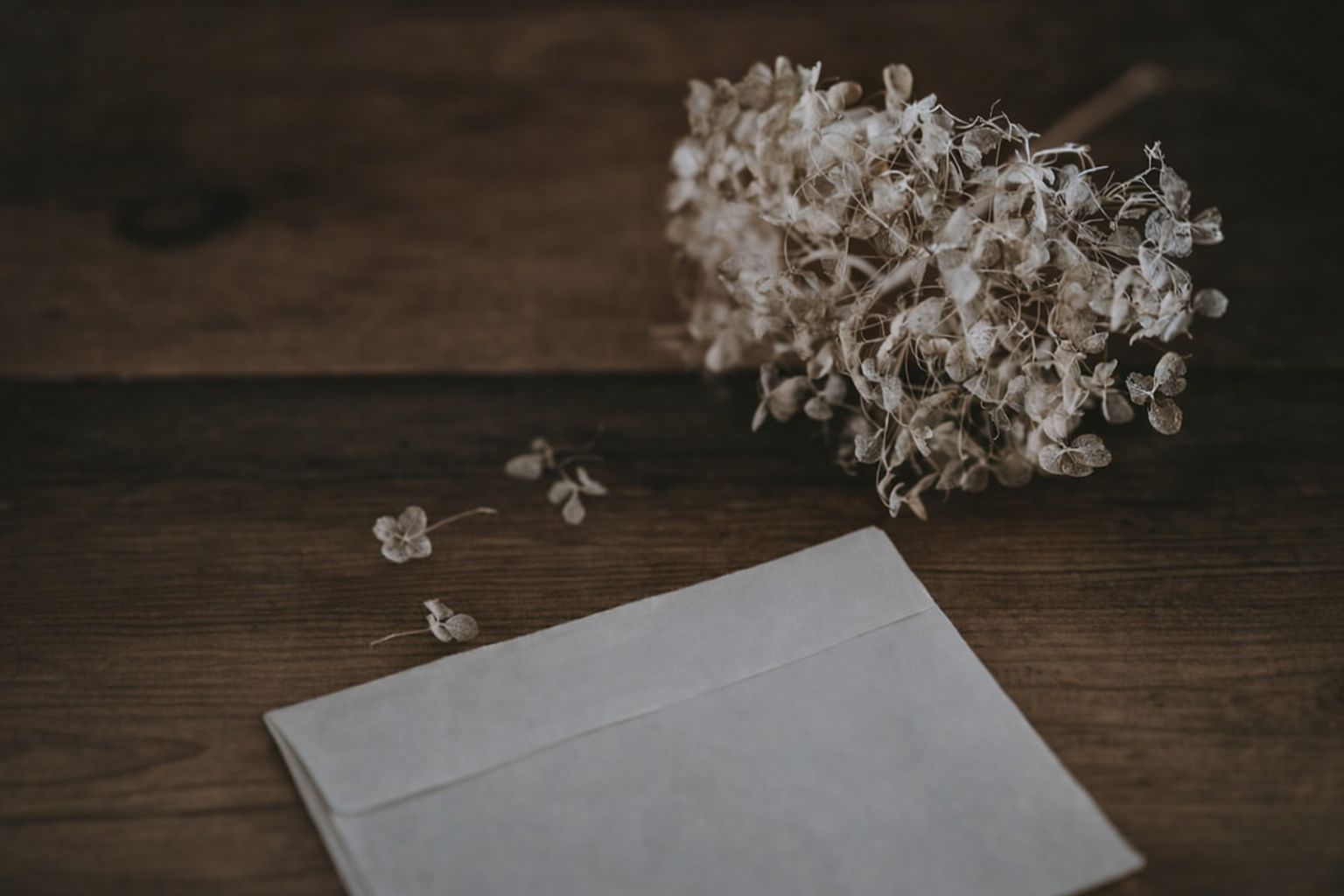 Ett tomt kuvert och torkade blommor på ett mörkt träbord, kan symbolisera dokument.